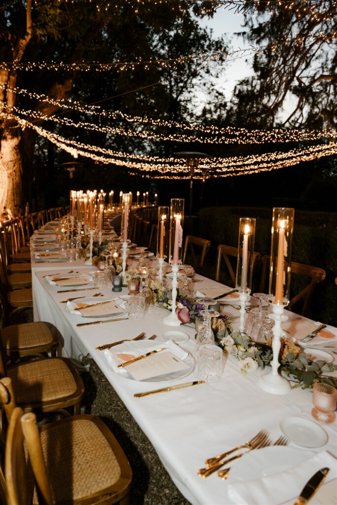 Een lange dinertafel met bruiloft decoratie en lichtsnoeren door de bomen